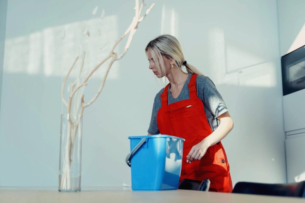 Reinigungskraft in orangefarbener Latzhose bei der Arbeit mit Putzeimer