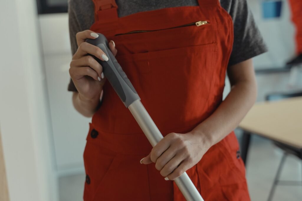 Reinigungskraft in orangefarbener Latzhose mit Wischmopp