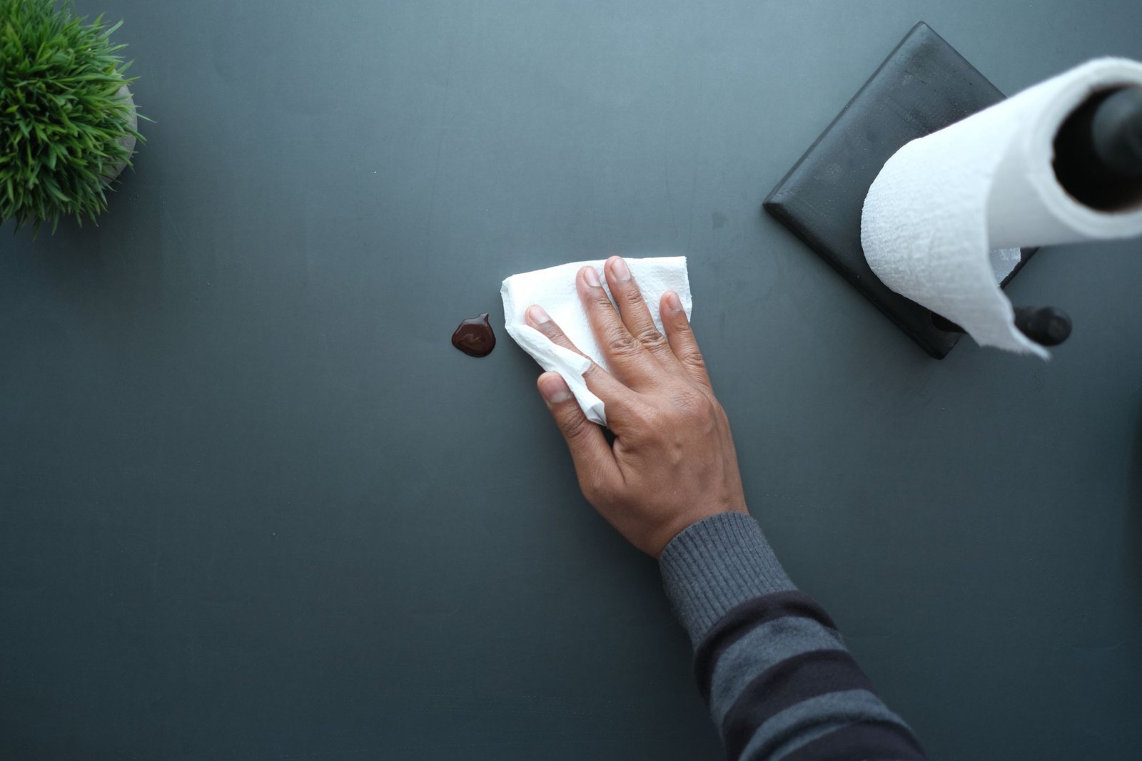 Hand wischt eine dunkle Schreibtischfläche mit einem Papiertuch ab
