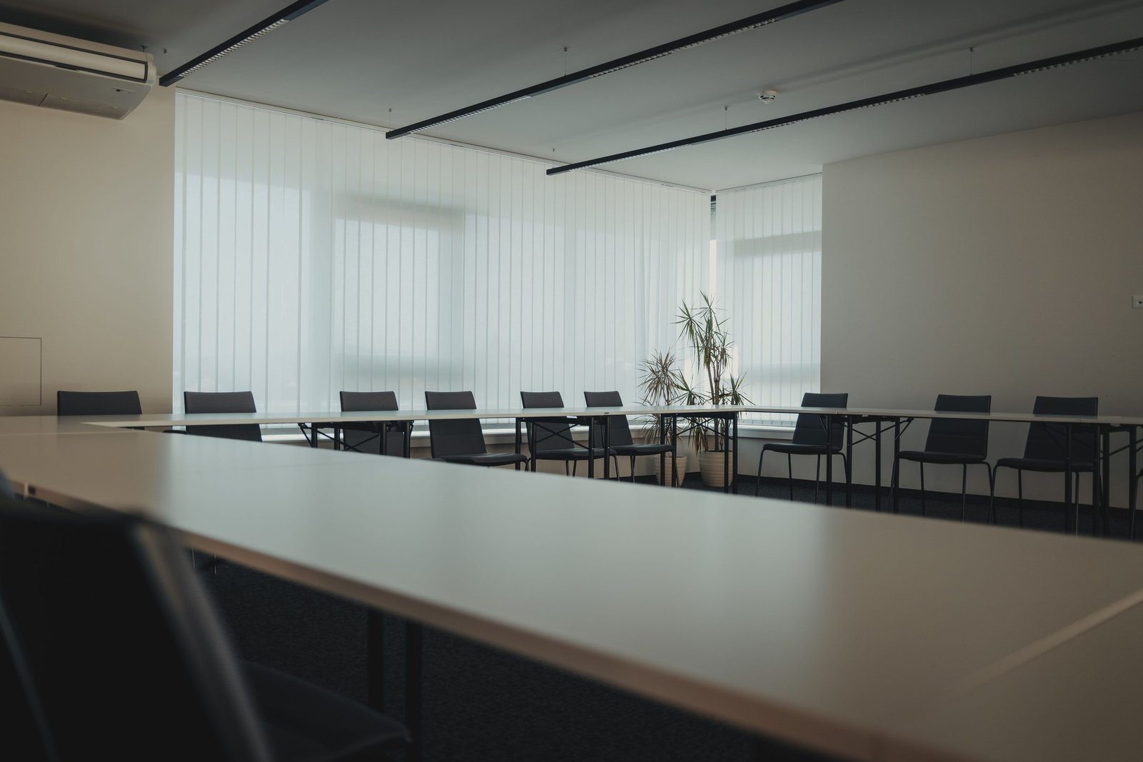 Aufgeräumter Besprechungsraum mit langen Tischen, Stühlen und Lamellenvorhängen in einem Bürogebäude